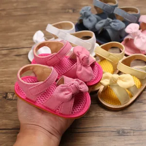 Mano sosteniendo sandalias rosas para bebé con lazo y suela de malla transpirable