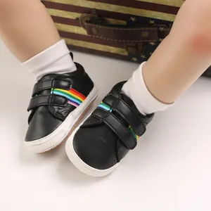 Détail de chaussures de marche noires pour bébé avec rayures arc-en-ciel et semelle souple