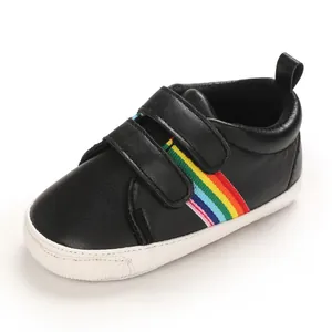 Détail d'une chaussure pour bébé noire avec rayures arc-en-ciel et semelle blanche