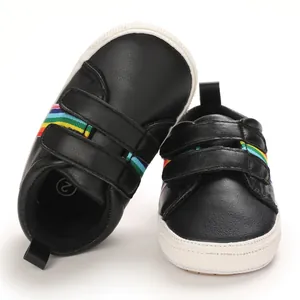 Gros plan de chaussures de marche pour bébé noires avec rayures arc-en-ciel et velcro