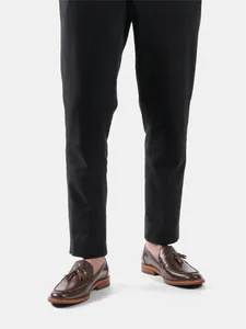 Close-up detail view of classic men's brown leather tassel loafers worn with black trousers