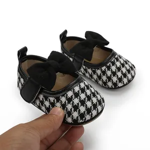 Nahaufnahme von Baby-Prinzessinenschuhen mit schwarz-weißem Hahnentrittmuster und Schleife
