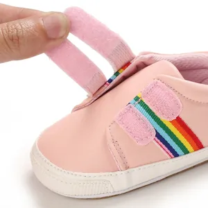 Détail du fermoir velcro sur des chaussures de marche roses pour bébé avec rayures arc-en-ciel