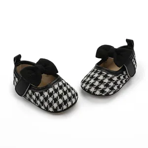 Nahaufnahme von Baby-Prinzessin-Schuhen mit schwarz-weißem Hahnentrittmuster und Schleife