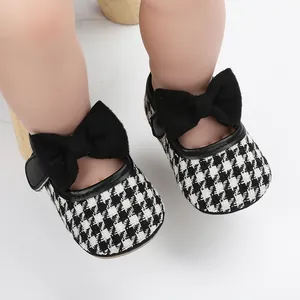 Nahaufnahme von Babyschuhen für Mädchen mit schwarz-weißem Hahnentrittmuster und Schleife