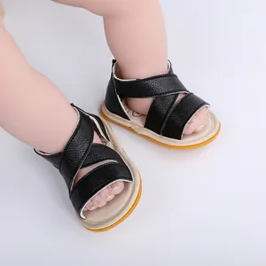 Détail de sandales d'été pour bébé avec lanières noires croisées et semelles en gomme.
