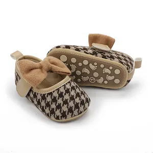 Nahaufnahme von Baby-Mädchen-Schuhen mit Hahnentrittmuster und weicher Plüschschleifen-Deko