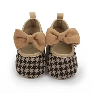 Detail von Baby-Prinzessinenschuhen mit Hahnentrittmuster und einer großen braunen Schleife.