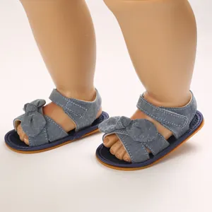 Detalle de sandalias vaqueras para bebé con lazo y suela de goma blanda para gatear.