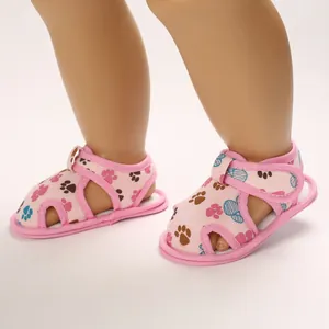 Primer plano de sandalias rosas para bebé con huellas de colores y velcro.