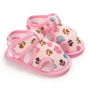 Primer plano de sandalias rosas para bebé con motivos de huellas y cierre de velcro