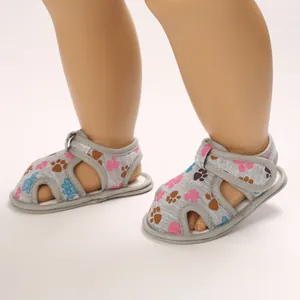 Primer plano de sandalias para bebé con huellas coloridas y cierre de velcro.