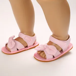 Primer plano de sandalias rosas para bebé con lazo y suela de goma blanda para verano.