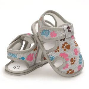 Detalle de sandalias grises para bebé con estampados de huellas de colores y cierre de velcro.
