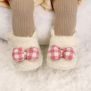 Κοντινό πλάνο από κρεμ βρεφικά μποτάκια fleece με ροζ καρό φιόγκους σε λευκό γούνινο χαλί.