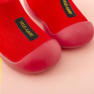 Detailansicht roter Baby-Socken-Schuhe mit SELF-CARE-Label und Gummischutz-Kappe.