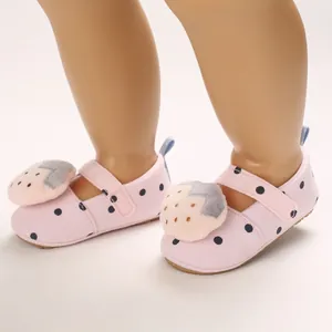 Close-up of pink polka dot baby walking shoes with strawberry plush on a doll's foot.
