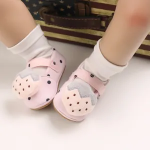 Close-up view of pink polka dot baby walking shoes with strawberry plush ornament