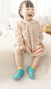 Süßes Kleinkind trägt türkis-gelbe Baby-Söckchenschuhe mit weicher Sohle im Schlafzimmer.