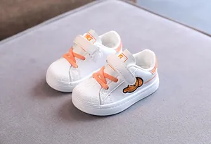 Detail view of white toddler sneakers with orange laces and shell-toe design