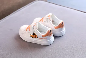 Detailed view of children's white shell-toe sneakers with orange embroidery and soft soles