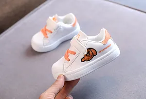 Close-up of children's white shell-toe sneaker with orange accents and embroidery.