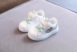 Macro view of white and green toddler shell-toe sneakers on a soft grey fabric surface