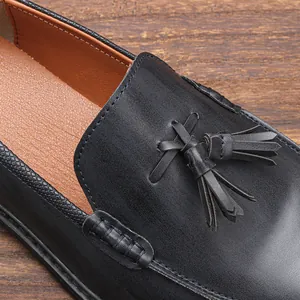 Close-up of black leather loafer with tassel detail and textured trim on wood background