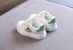 Detailed view of kids white shell-toe shoes with green accents and Velcro straps
