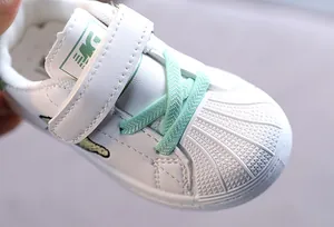 Detailed close-up view of children's white shell-toe sneakers with mint green laces