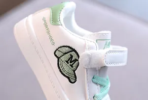 Close-up of white children sneakers with green accents and baseball cap embroidery design