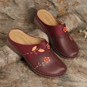 Close-up of maroon closed-toe floral mules with contrast stitching on rock background
