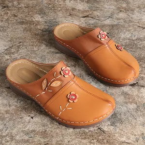 Close-up of brown closed-toe mules with decorative flower appliques and white stitching