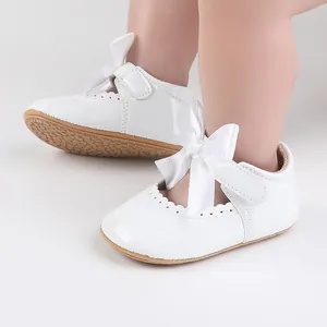 Nahaufnahme von weißen Lackleder-Babyschuhen mit großen Satinschleifen