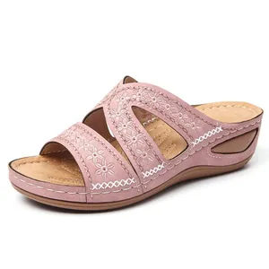 Gros plan de sandales compensées roses avec broderies florales et design peep toe.