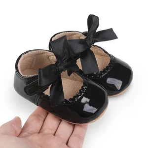 Nahaufnahme von glänzenden schwarzen Lackleder-Babyschuhen mit großer Satinschleife