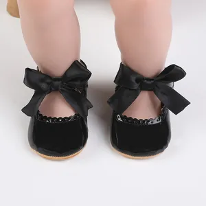 Detailansicht schwarzer Lackbabyschuhe mit großer Satinschleife und Wellenrand