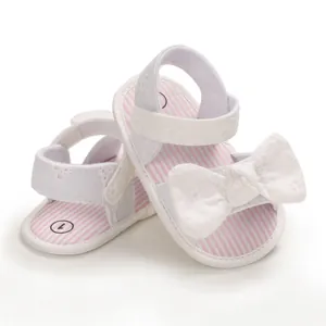 Primo piano di sandali bianchi per bambina con strisce rosa e fiocco delicato