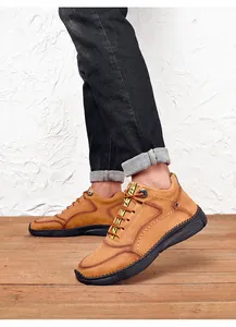 Detail view of men's tan leather casual shoes worn with black jeans on wooden floor.