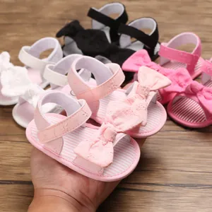 Primo piano di sandali rosa per neonata con fiocco ricamato e suola morbida a righe