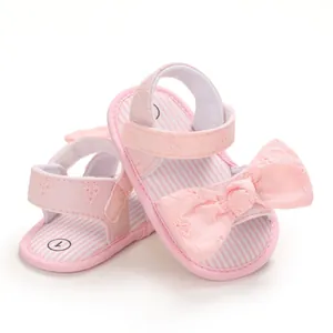 Dettaglio di sandali rosa per neonata con ricami floreali e un grande fiocco