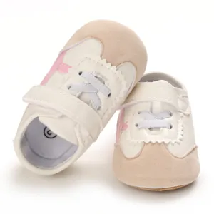 Close-up view of stylish white baby walking shoes with soft soles and pink decorative accents