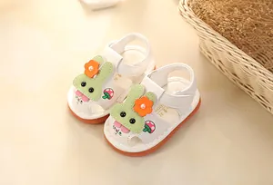 Close-up of white baby sandals with cute green bunny ears and orange flower detail