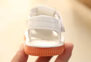 Macro view showing the heel strap and orange non-slip sole of this infant white sandal