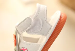 Close-up macro detail of soft white baby sandal showing velcro strap and textured orange sole