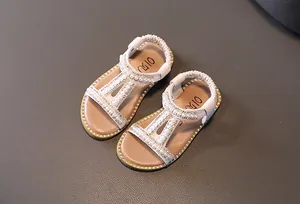 Elegant girls Roman sandals with pearls and rhinestones on a grey textured background.