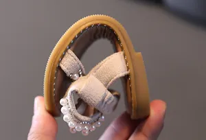 Close-up of flexible girl's sandal with pearl and rhinestone details and soft sole.