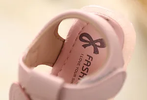 Close-up detail of soft pink leather baby sandal with bow logo and neat stitching