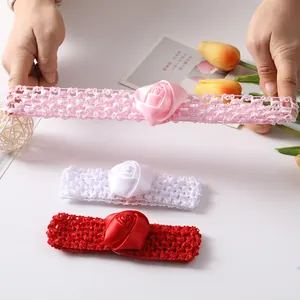 Detailweergave van drie gehaakte babyhoofdbanden met satijnen rozen in roze, wit en rood.