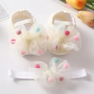 Close-up detail of cream-colored baby princess shoes and matching pom-pom headband set